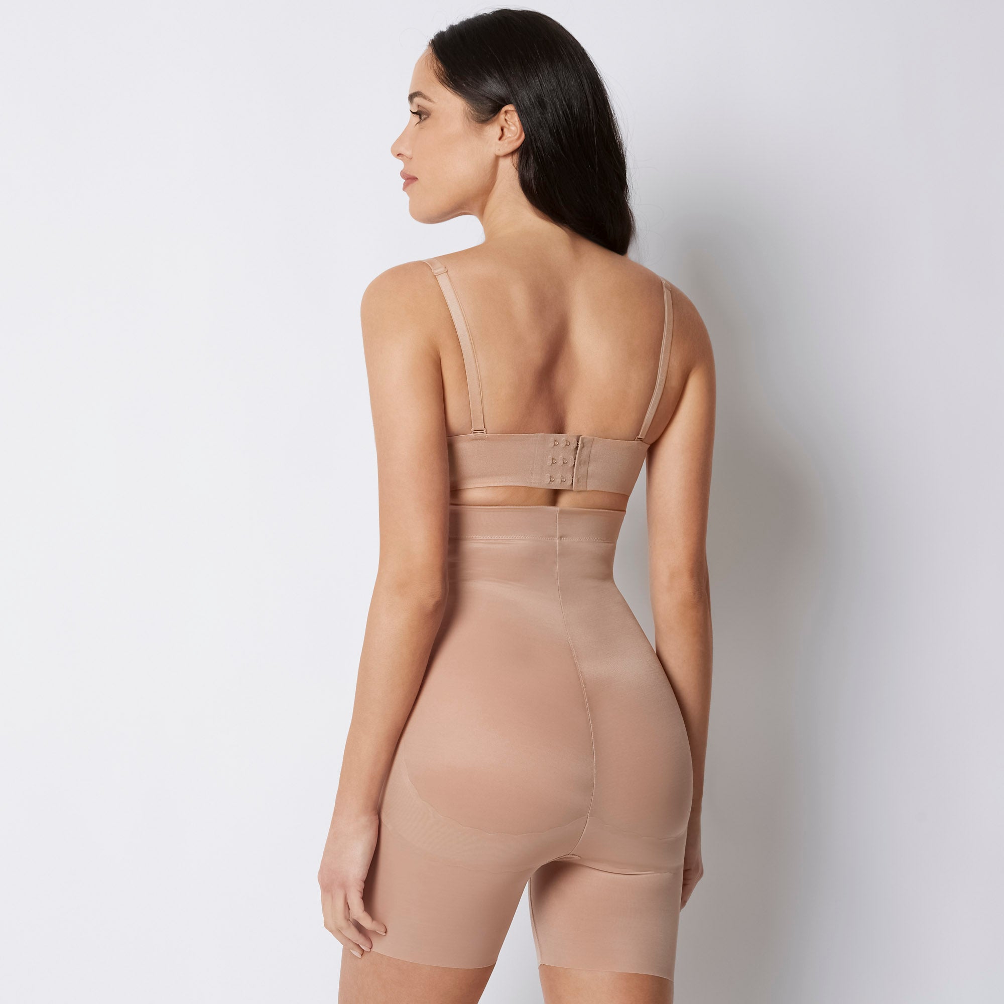 Woman wearing a beige shapewear bodysuit against a white background